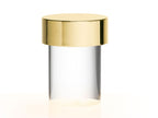 Close view of this Clérachic lamp on white, with a gold cap over a clear smooth glass body and a warm glow at the foot.