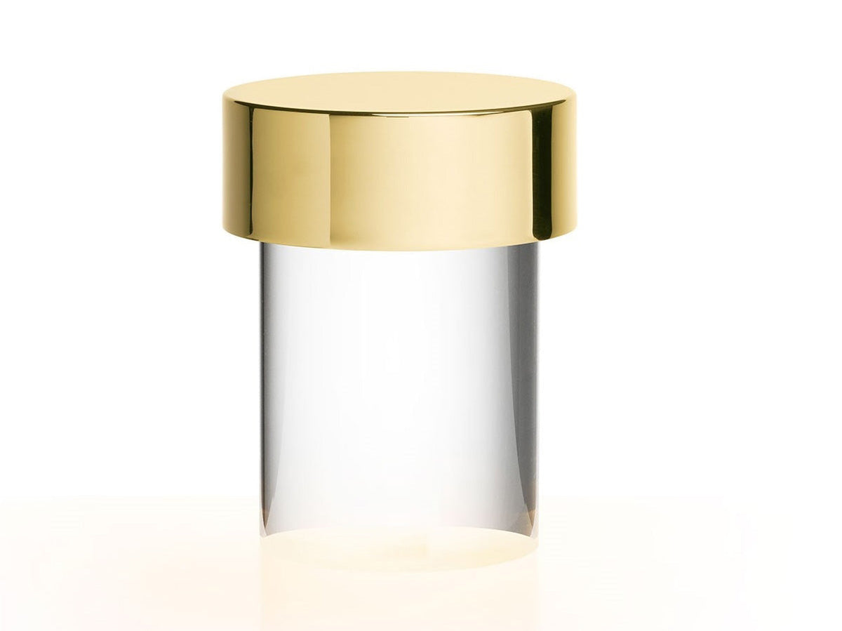 Close view of this Clérachic lamp on white, with a gold cap over a clear smooth glass body and a warm glow at the foot.