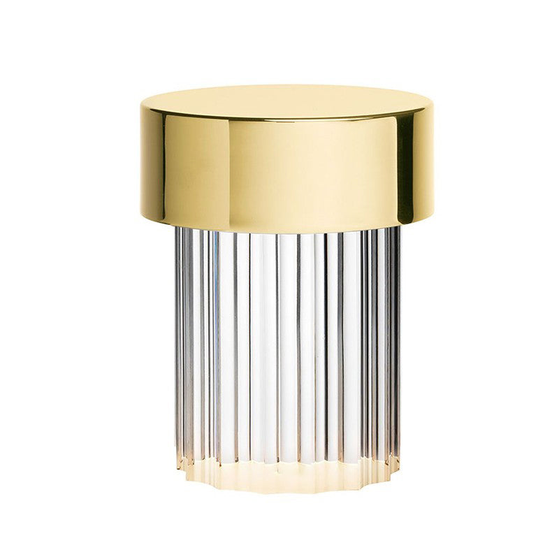 Close view of a Clérachic lamp with a polished gold cap and vertical flutes in the clear glass body, on white.