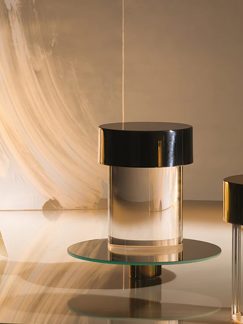 A Clérachic lamp with a black cap and clear glass sitting on a round glass tray in a warm, brushstroke-lit set.