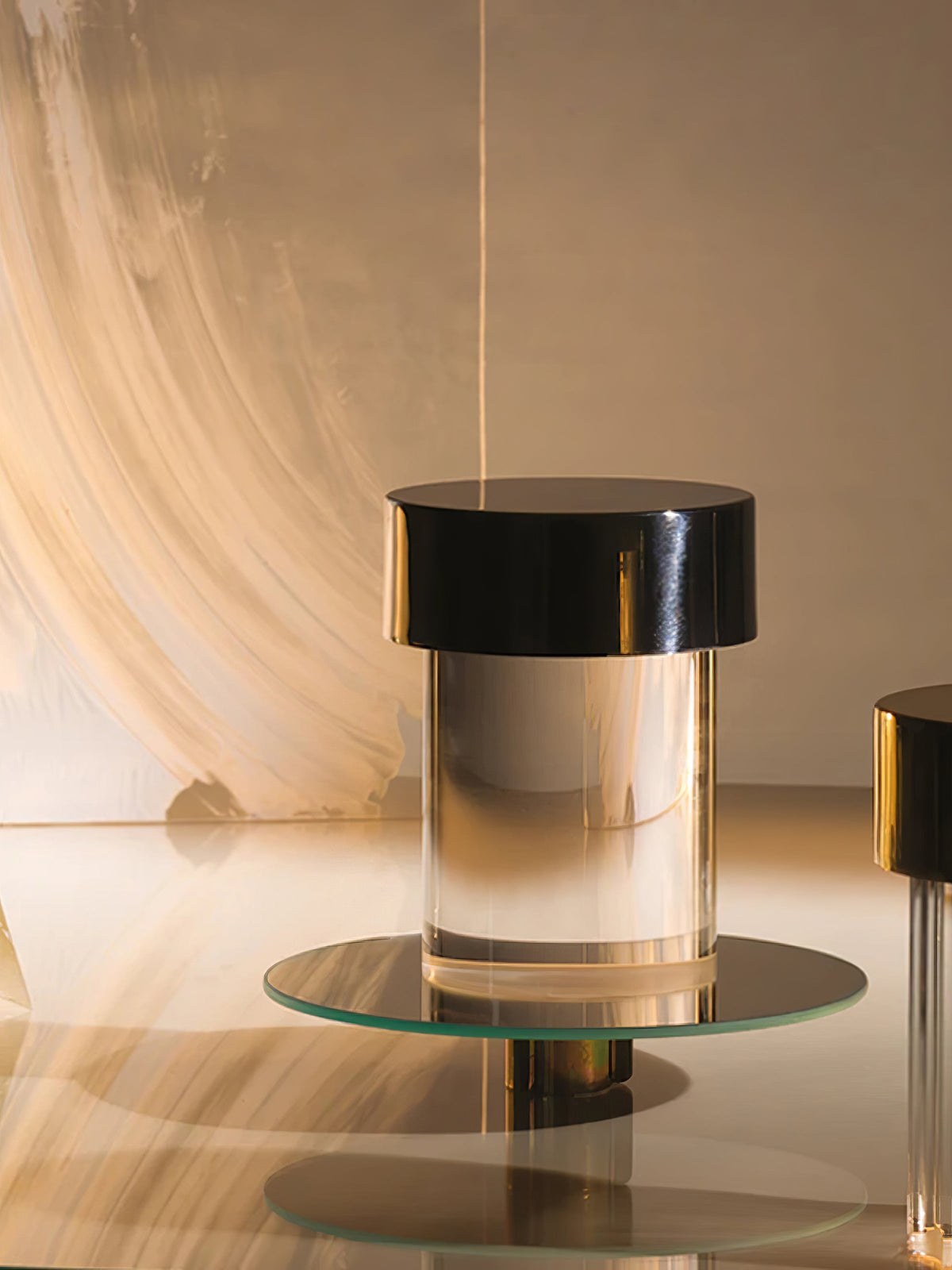 A Clérachic lamp with a black cap and clear glass sitting on a round glass tray in a warm, brushstroke-lit set.