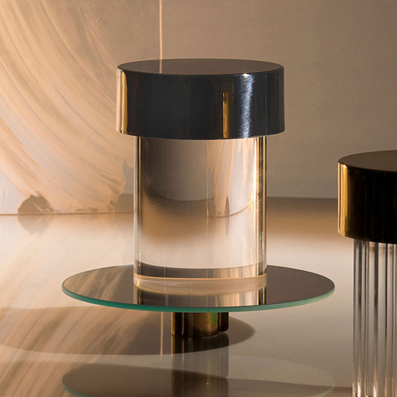 Close view of a Clérachic lamp with a black cap and clear glass body on a round glass tray, with warm light behind.