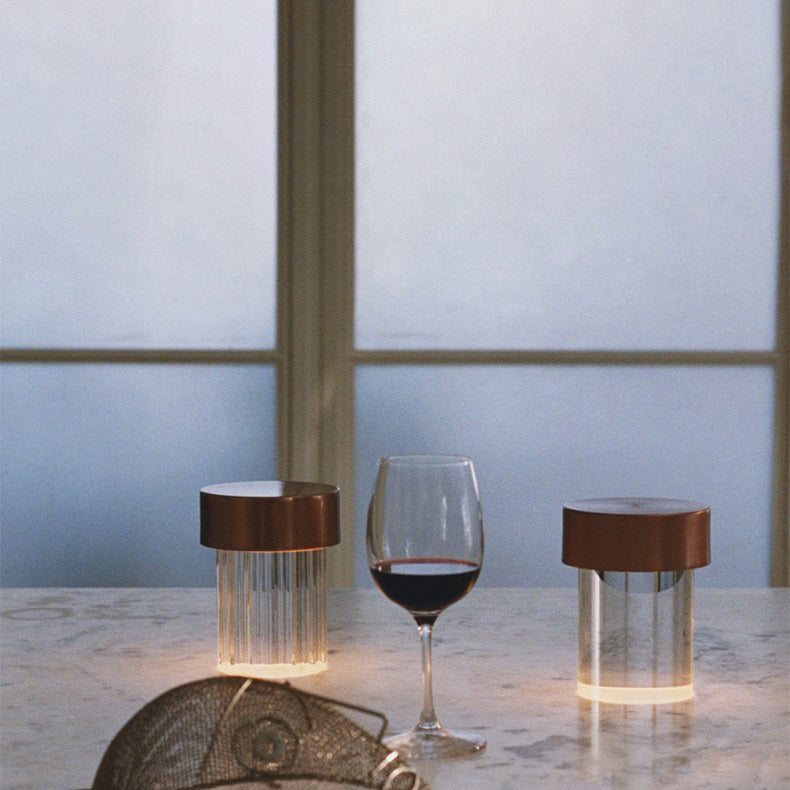 Two Clérachic lamps with dark copper caps on a marble counter, one fluted and one smooth, beside a glass of red wine.