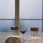 Two Clérachic lamps with dark copper caps on a marble counter, one fluted and one smooth, beside a glass of red wine.