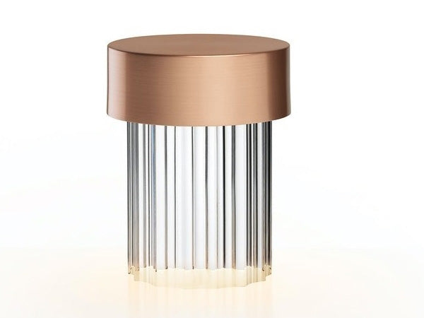 A fluted-glass Clérachic lamp with a brushed rose gold cap on white, with a soft warm light at the base.