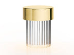 Large view of a fluted-glass Clérachic lamp with a polished gold cap on white, with a warm glow at its foot.