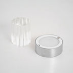 The Clérachic lamp taken apart on a pale surface, with the fluted glass sleeve beside the chrome base and its round light panel.