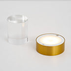 The gold base of this Clérachic lamp switched on, its round panel glowing, beside the separate clear glass cylinder.