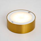 Close view of the round light panel in the gold base of this Clérachic lamp, glowing warm white with a small touch sensor at the rim.