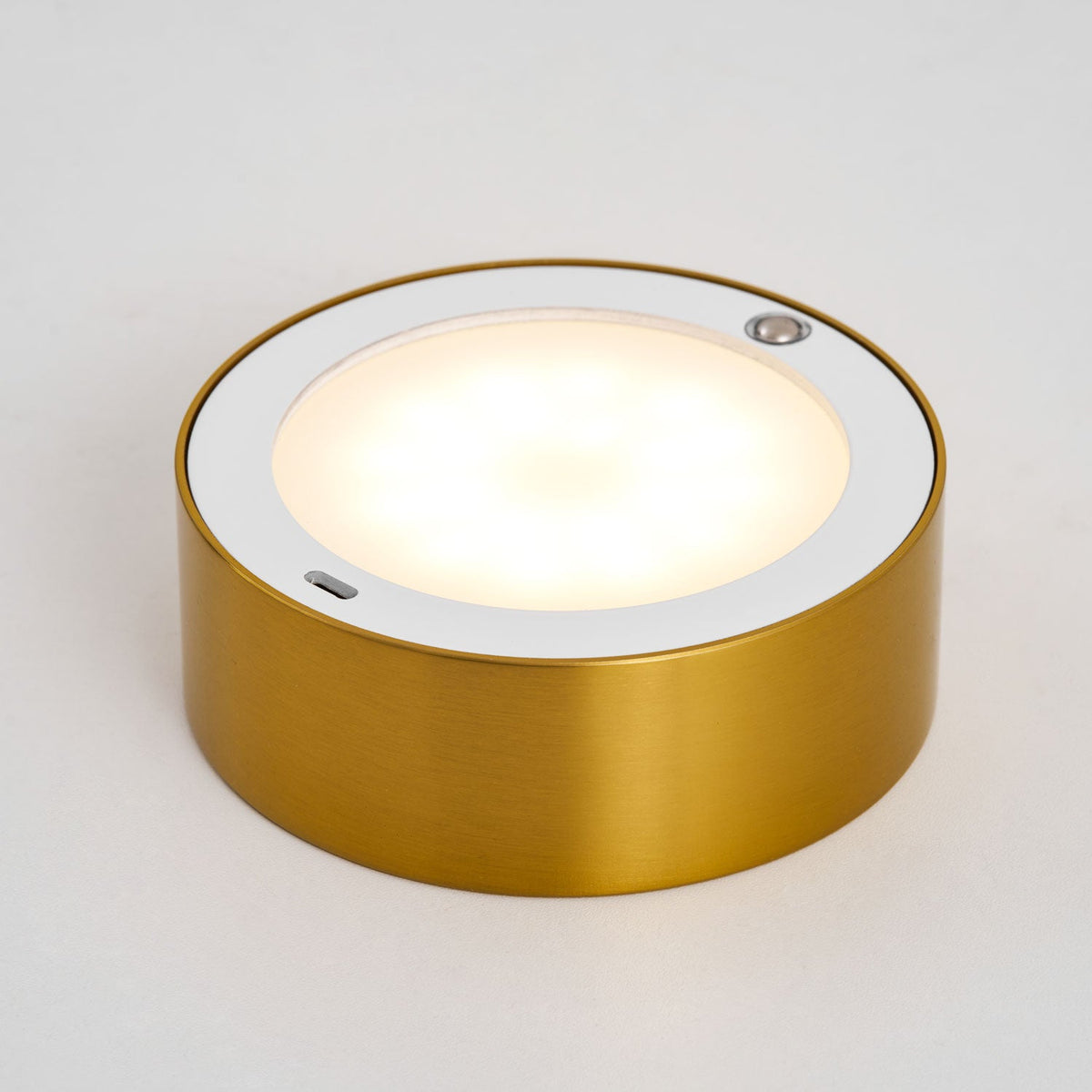 Close view of the round light panel in the gold base of this Clérachic lamp, glowing warm white with a small touch sensor at the rim.