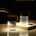 Two Clérachic lamps lit on a marble table with a book, one fluted with a black cap and one smooth with a dark copper cap.