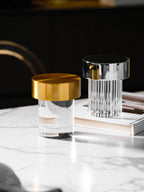 Tall crop of two Clérachic lamps on a white marble table, a smooth gold-capped one in front of a fluted chrome-capped one.