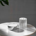 The chrome base of this Clérachic lamp lying open beside its fluted glass sleeve on a round marble-topped table.