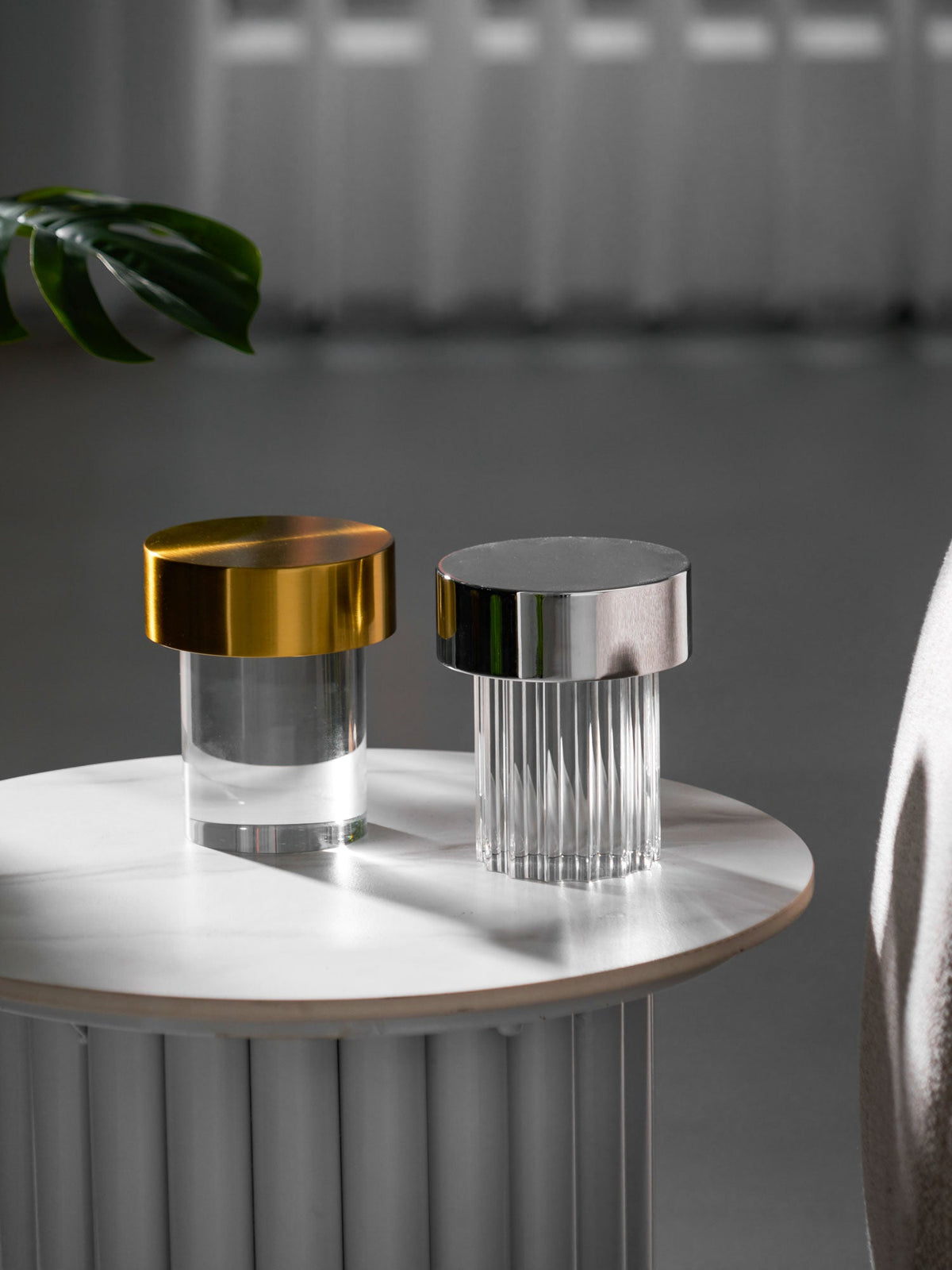 Tall crop of two Clérachic lamps on a round marble-topped table, a gold-capped smooth one and a chrome-capped fluted one.