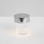 A fluted Clérachic lamp with a chrome cap lit at the base on a pale tabletop, seen from slightly above.