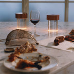 Two Clérachic lamps with dark copper caps glowing on a marble counter next to a glass of red wine and a wire basket.