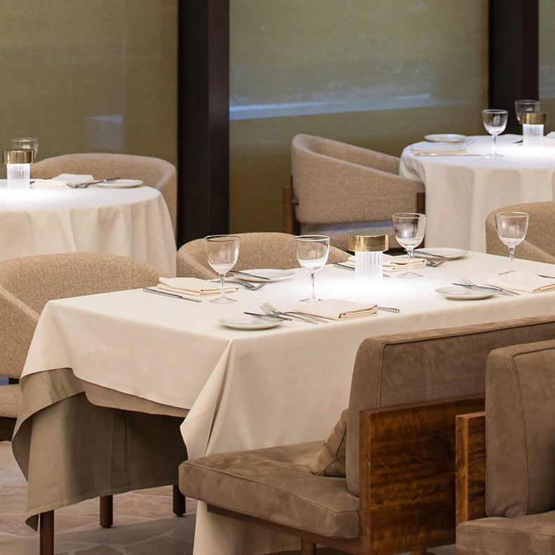 A lit Clérachic lamp on a white-clothed table in a restaurant dining room, with wine glasses and brown upholstered chairs around it.