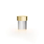 A Clérachic lamp with a gold cap and ribbed clear glass on white, with a soft warm glow beneath it.