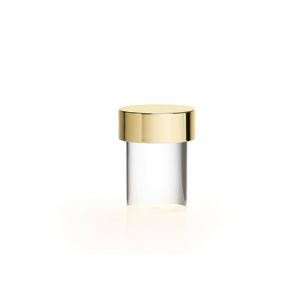 This Clérachic lamp on white, with a small gold cap and a clear smooth glass body above a faint warm glow.