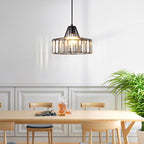 Lit black Clérachic drum pendant with clear crystal prisms hangs over a pale wooden dining table with a decanter, in front of panelled walls.