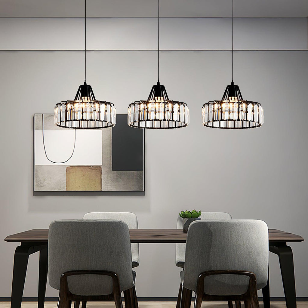 Three black-framed Clérachic crystal drum pendants in a row over a dark dining table with grey chairs, in front of a large abstract print.
