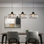 Three black-framed Clérachic crystal drum pendants in a row over a dark dining table with grey chairs, in front of a large abstract print.