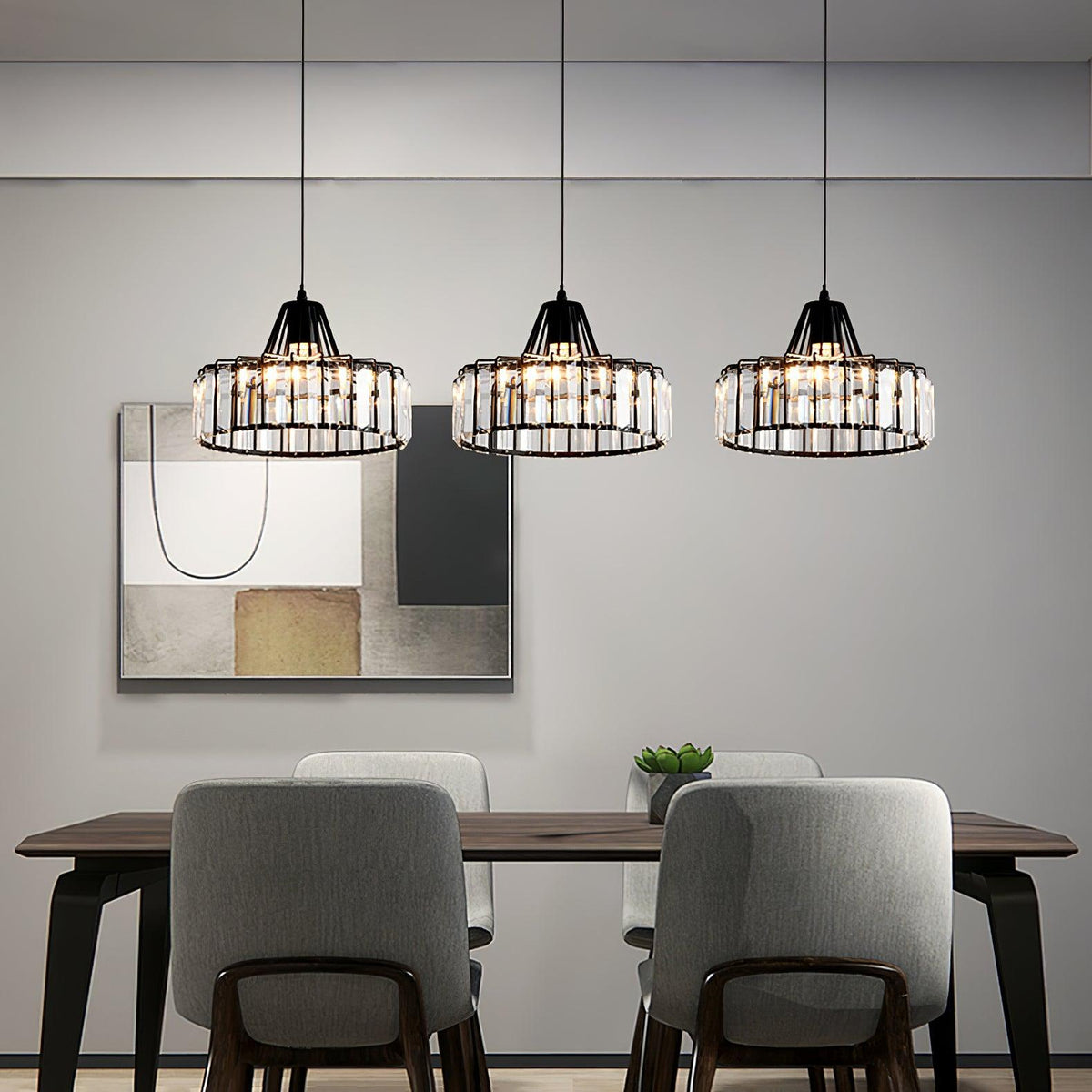 Three black-framed Clérachic crystal drum pendants in a row over a dark dining table with grey chairs, in front of a large abstract print.