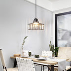 Black-framed crystal drum pendant from Clérachic, lit, hanging in a white dining room above a table set with plates and a woven runner.