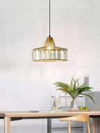 Gold crystal drum pendant from Clérachic hanging in a pale room above a wooden table, with a fern and a jug on the counter behind.