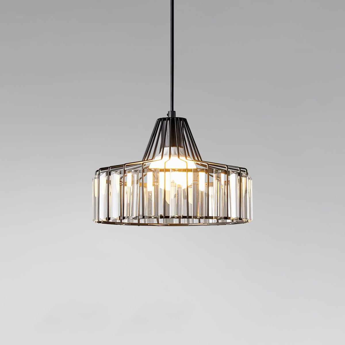 Close view of a black wire-framed crystal drum pendant from Clérachic, with its bulb glowing against a soft grey gradient.