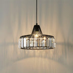 Warm light spills from this black Clérachic crystal drum pendant, throwing prism shadows across the wall and ceiling behind it.