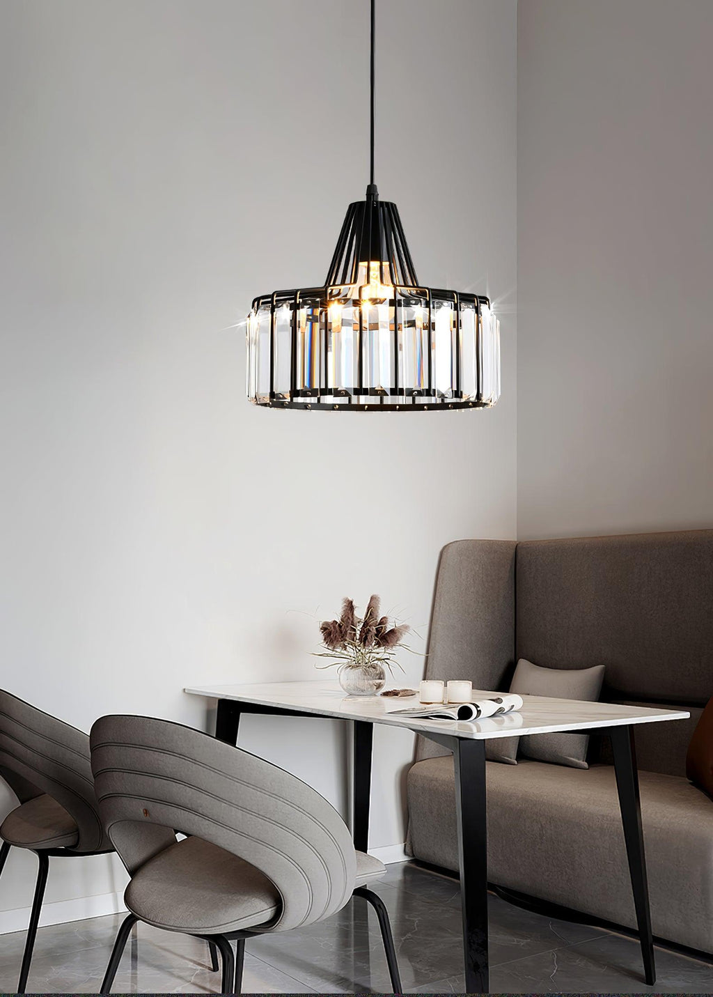 Small black-framed crystal drum pendant from Clérachic above a white table, with a grey sofa and moulded chairs in a neutral room.