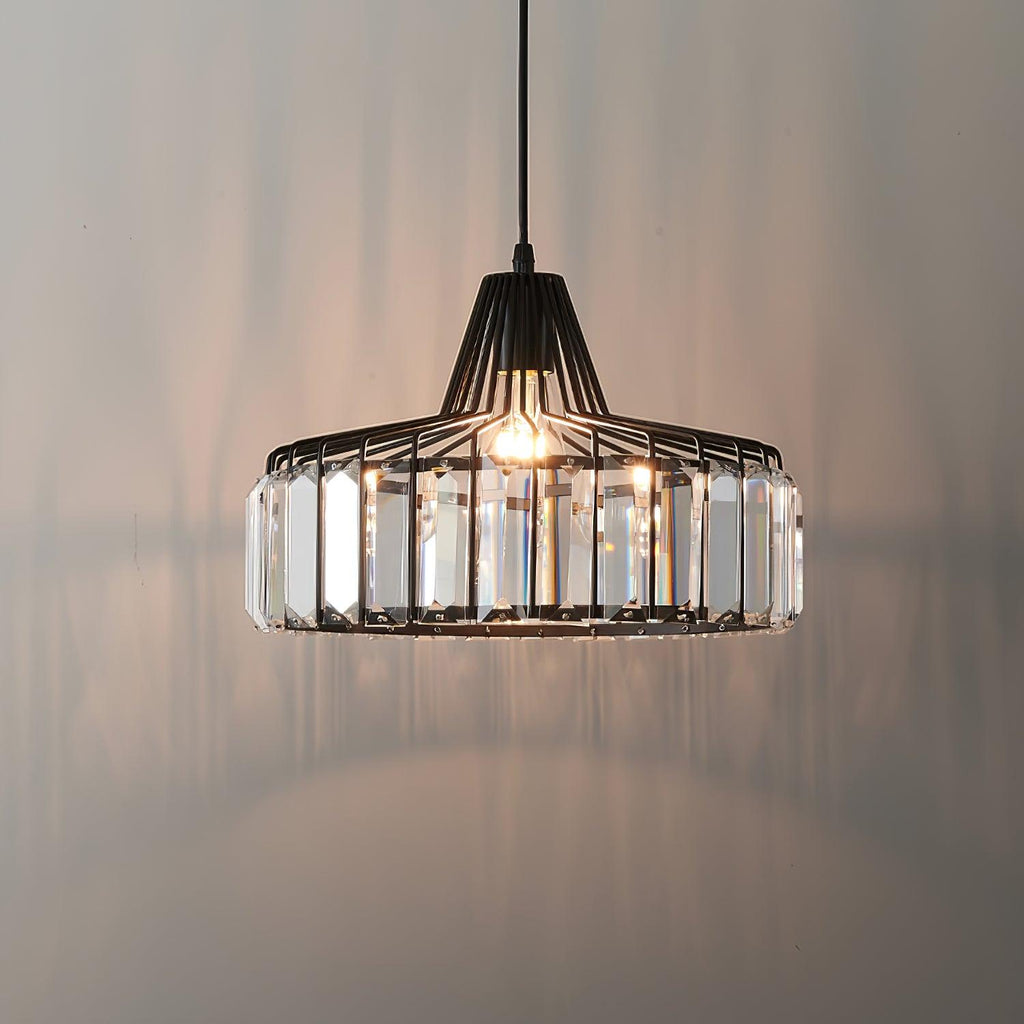 Lit black wire-framed crystal drum pendant from Clérachic, casting soft reflections on a warm grey wall behind it.