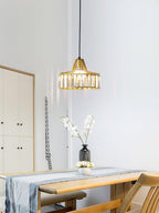 A gold crystal drum pendant from Clérachic hangs by a white cabinet, with a vase of blossom on a wooden table below.
