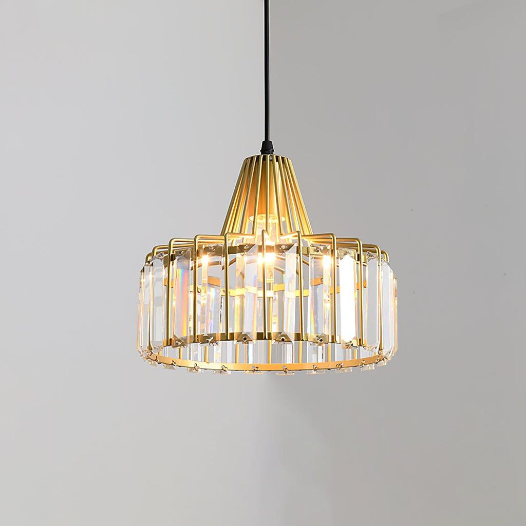 Gold wire-framed crystal drum pendant from Clérachic, lit, with clear prisms around the drum, against a soft grey wall.