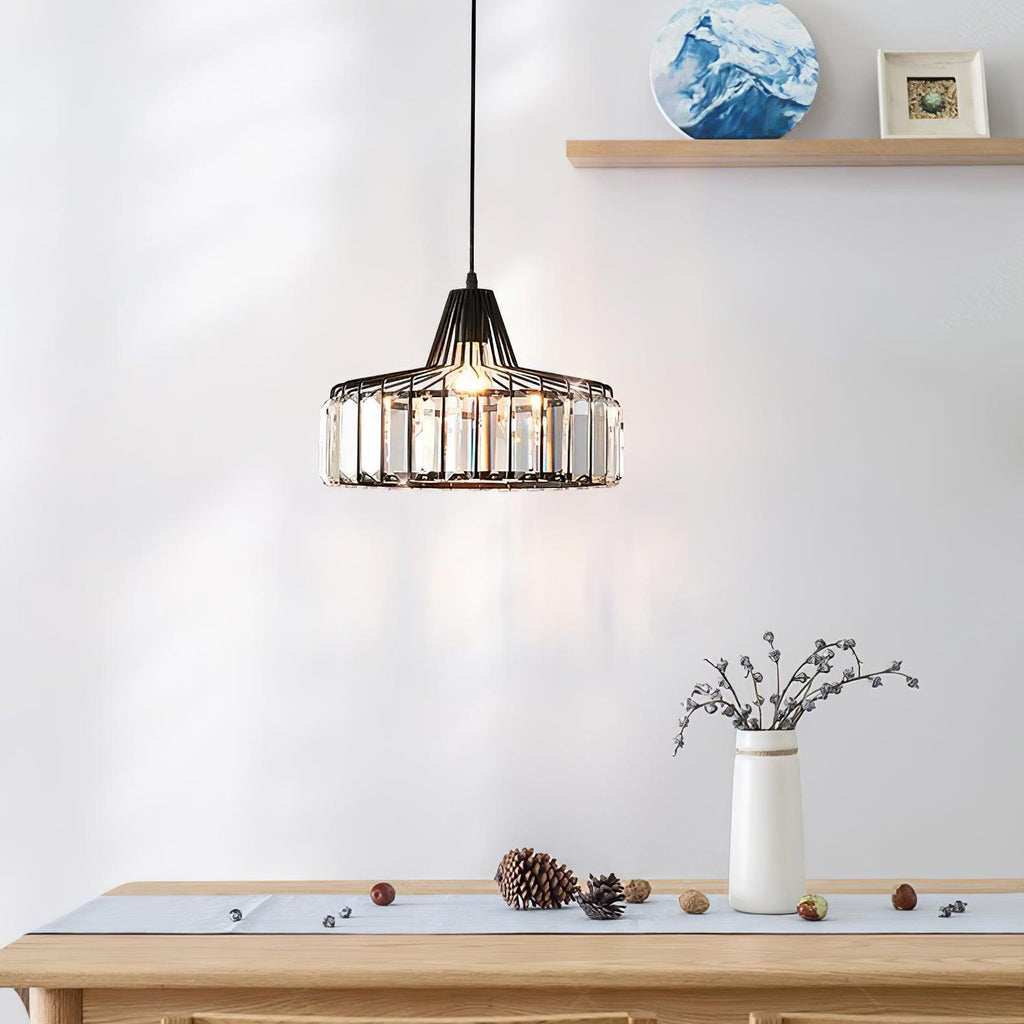 Black crystal drum pendant from Clérachic hanging in front of a pale wall, with a shelf, a vase of twigs and pine cones on the table below.