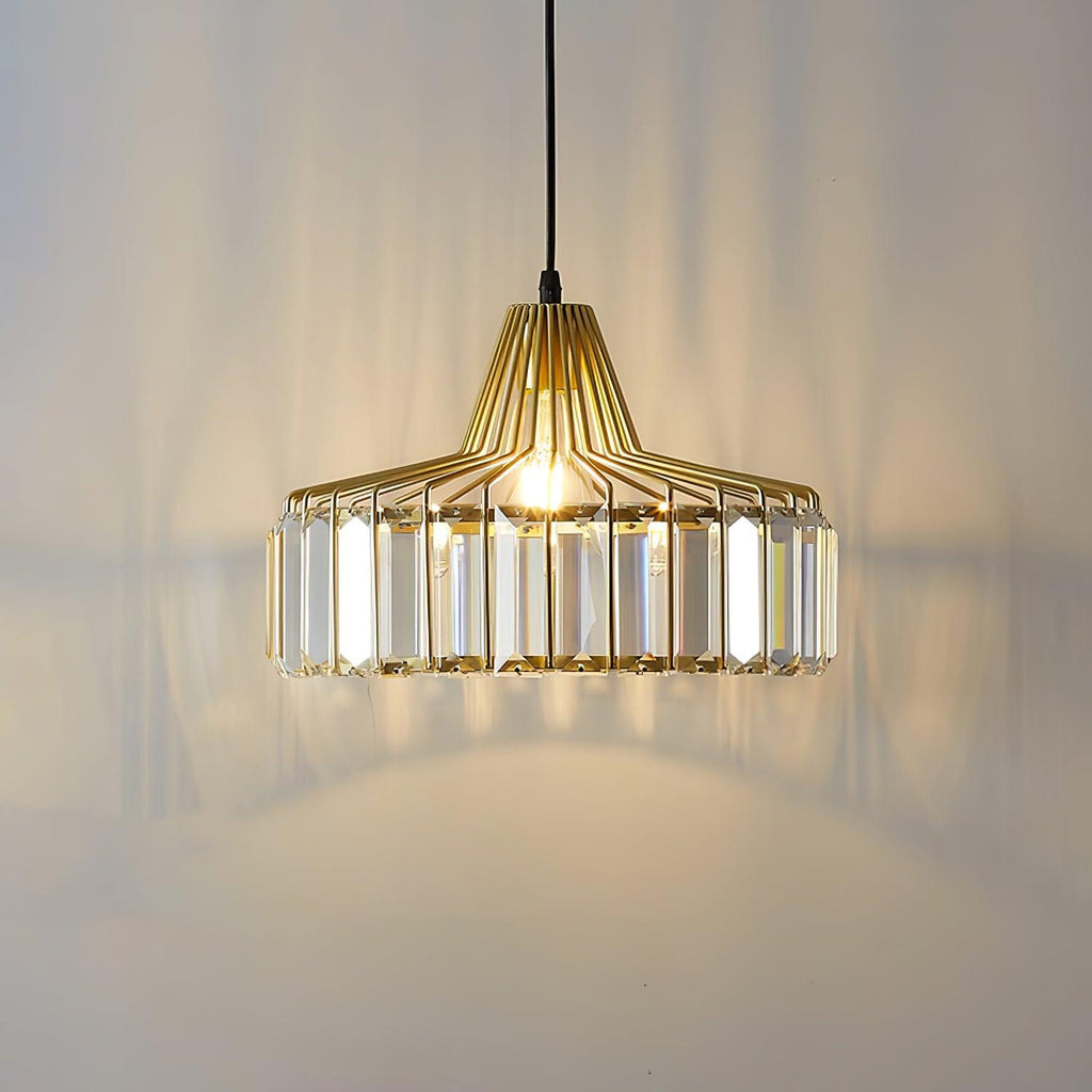 Lit gold crystal drum pendant from Clérachic, with warm light and long prism shadows across the wall behind it.