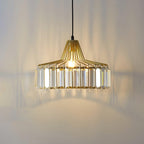 Lit gold crystal drum pendant from Clérachic, with warm light and long prism shadows across the wall behind it.