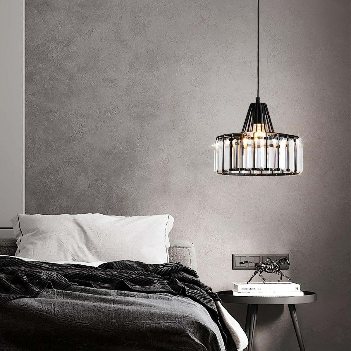A black Clérachic crystal drum pendant hangs above a bed with dark linen and a round side table, against a textured grey wall.