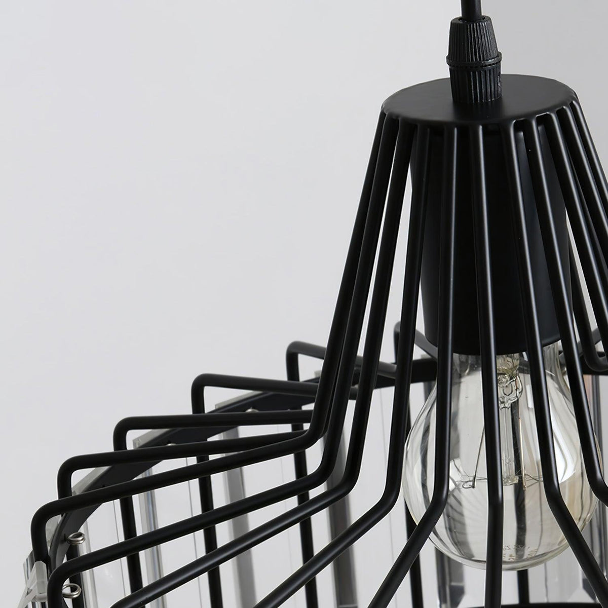 Close view of the black wire cage, cable gland and clear bulb of this Clérachic crystal drum pendant, against a soft grey wall.