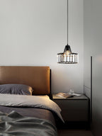 Small black crystal drum pendant from Clérachic hung beside a bed with tan leather headboard, grey bedding and a dark bedside table.