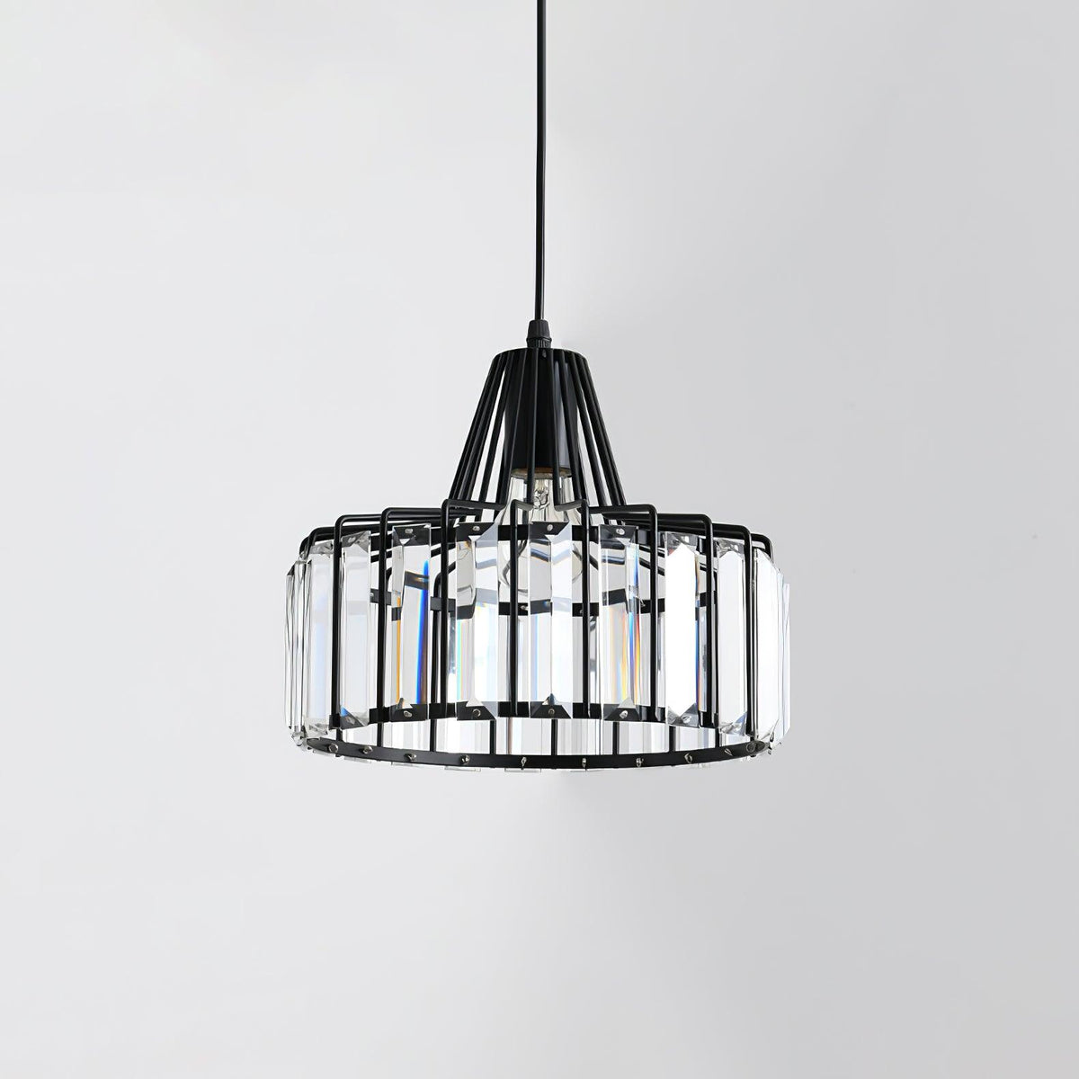 Black wire-framed Clérachic pendant with tall clear crystal prisms around the drum, unlit, against a pale grey wall.