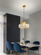 A gold crystal drum pendant from Clérachic on a brass ceiling plate hangs in a grey dining room with navy velvet chairs and a marble table.