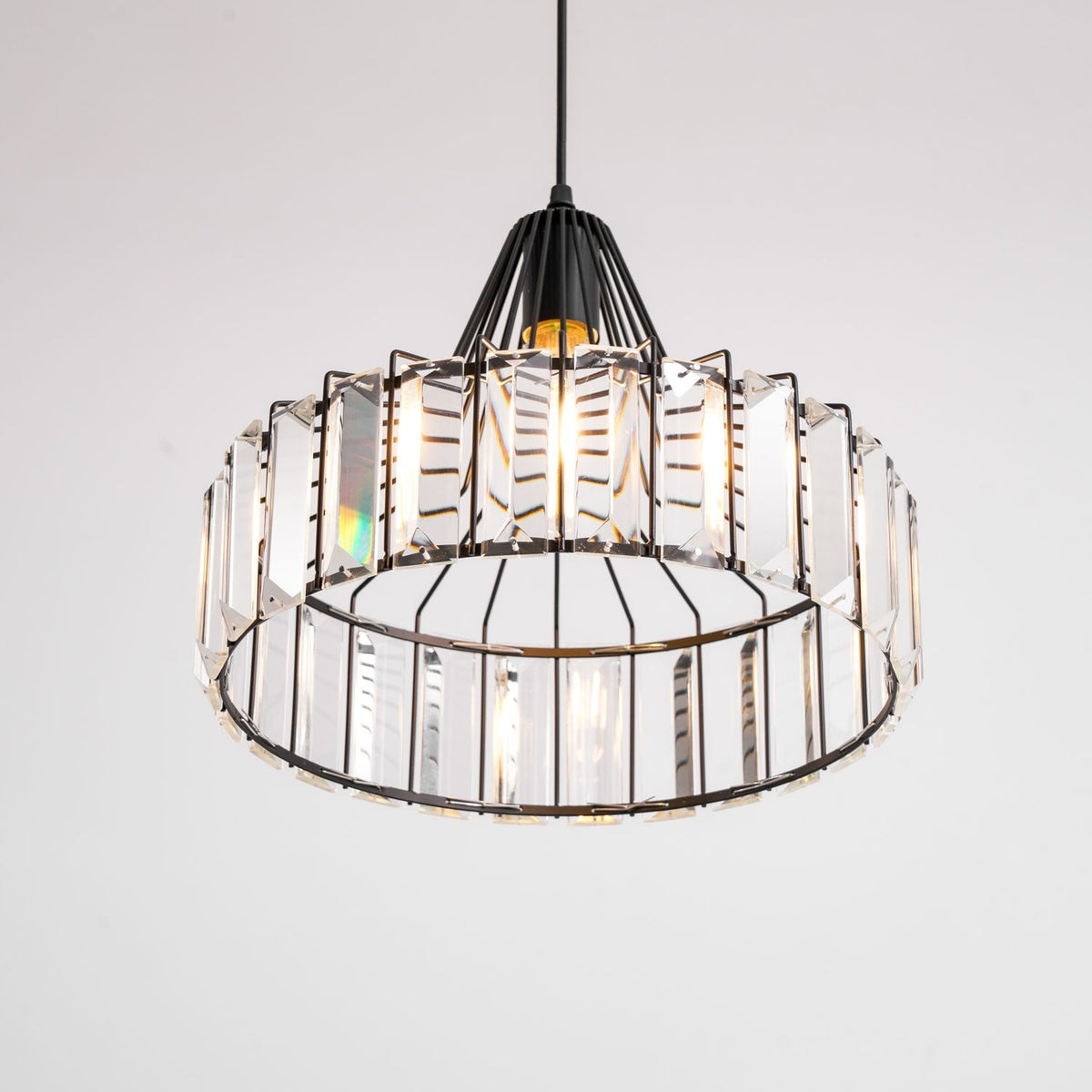 Upward view into the black drum pendant from Clérachic, showing the open base and the clear prisms ringed around the frame.