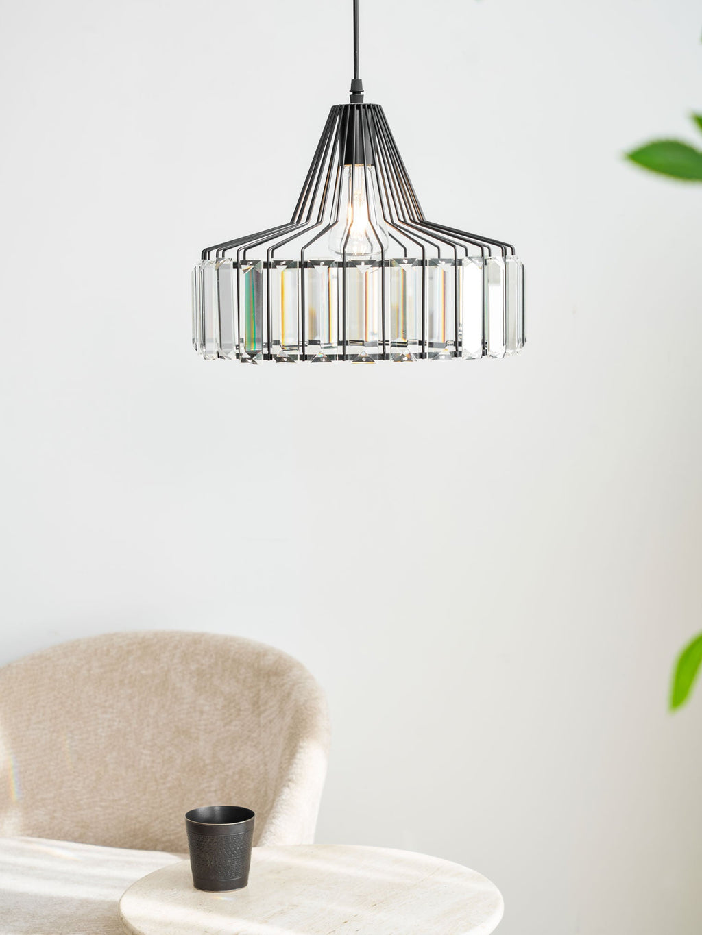 A black wire-framed Clérachic crystal drum pendant hangs high in a bright corner, with a beige armchair and a green plant to one side.