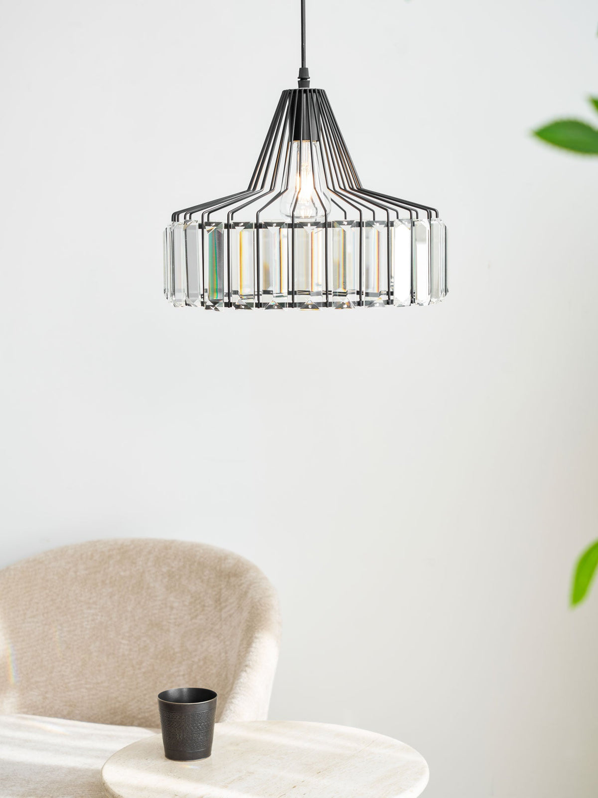 A black wire-framed Clérachic crystal drum pendant hangs high in a bright corner, with a beige armchair and a green plant to one side.