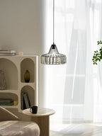 A lit black crystal drum pendant from Clérachic hangs by sheer white curtains, with a shelf unit, books and a black mug on a stone table below.