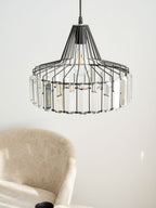 Close view of the black cage and clear prisms of this Clérachic pendant, with a beige chair and a mug softly blurred behind.