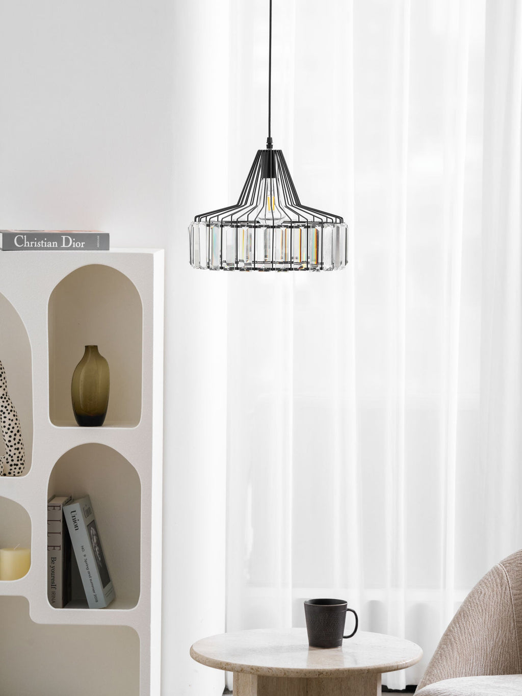 Small black crystal drum pendant from Clérachic hangs high in a bright corner, above an arched shelf and a round wooden table with a cup.