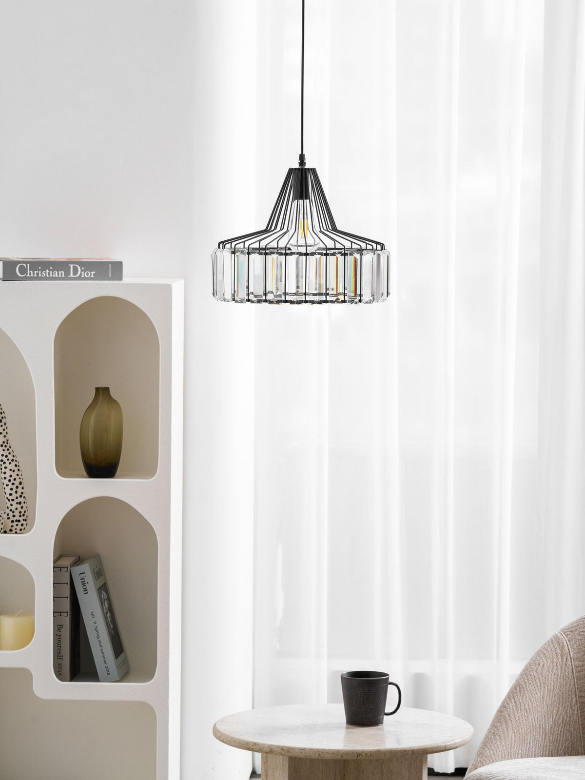 Small black crystal drum pendant from Clérachic hangs high in a bright corner, above an arched shelf and a round wooden table with a cup.